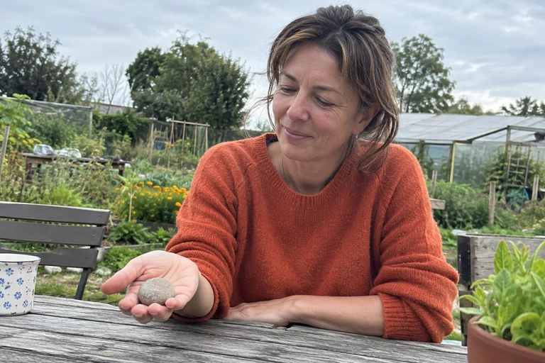 Une femme tient un galet dans sa paume dans un jardin
