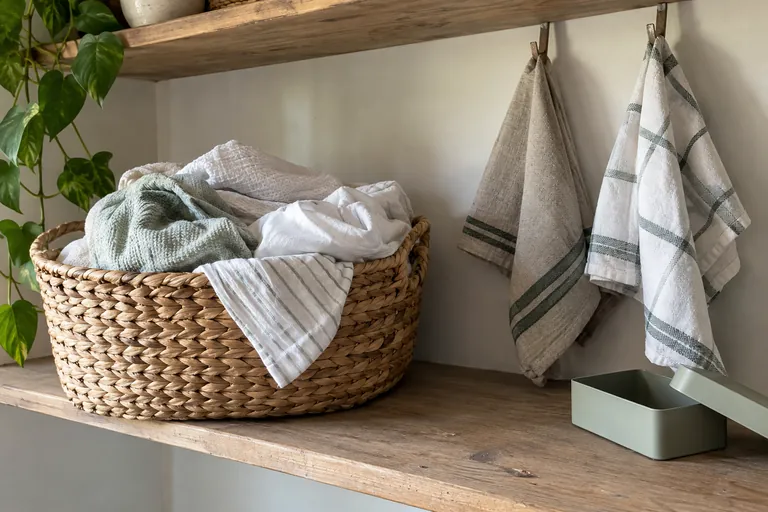 Un panier de linge et une boîte ouverte reposent sur une étagère sous des torchons suspendus.