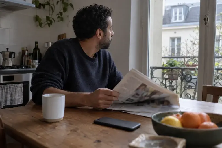 Un homme referme son journal et regarde vers une fenêtre