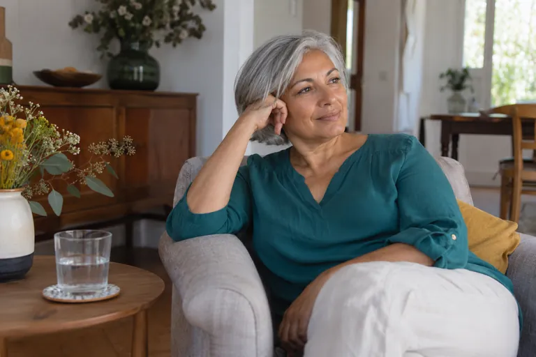 Une femme aux cheveux gris se repose dans un fauteuil près d’un verre d’eau