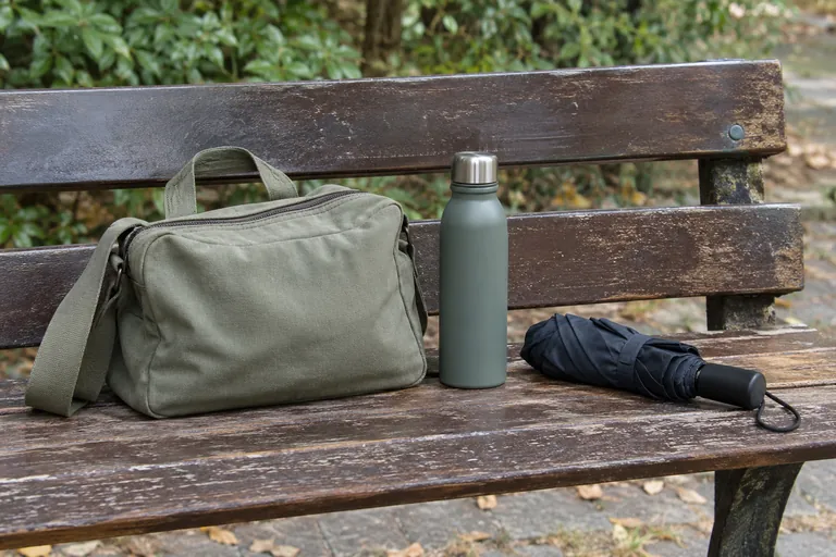 Un sac fermé, une gourde et un parapluie plié reposent sur un banc.