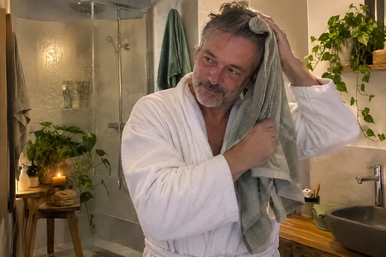 Un homme en peignoir se sèche les cheveux avec une serviette dans une salle de bains tamisée