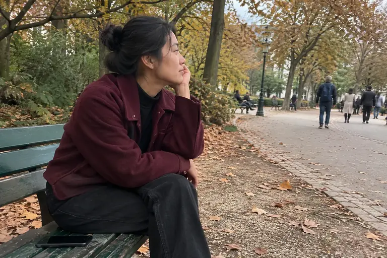 Une femme regarde le parc, son téléphone posé à côté sur le banc