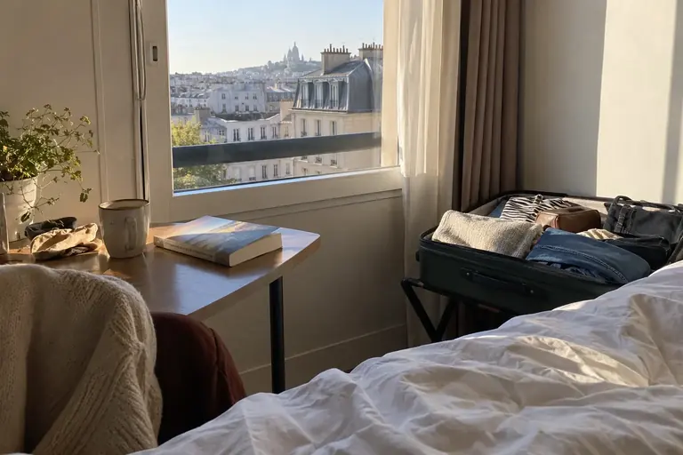Une valise partiellement défaite près d’une fenêtre d’hôtel éclairée par le jour, avec quelques vêtements et un livre
