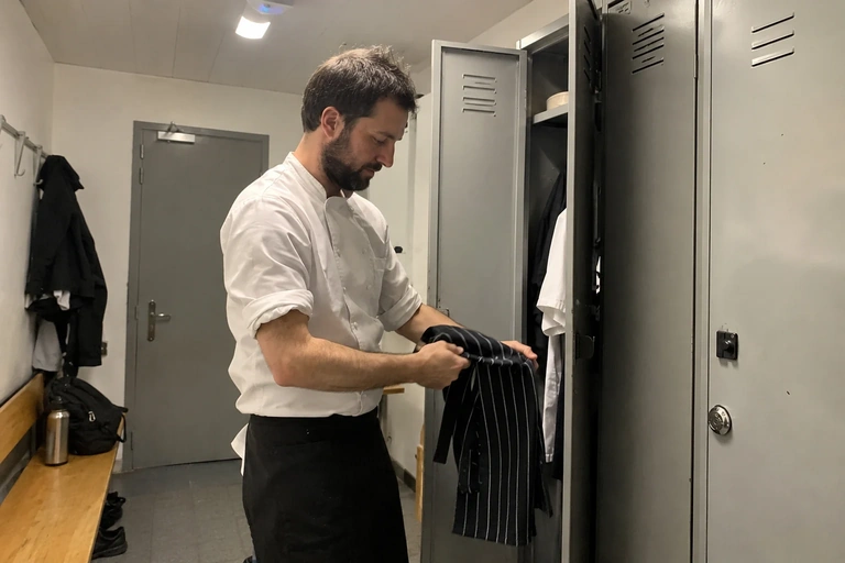 Un homme range son tablier dans un vestiaire après son travail