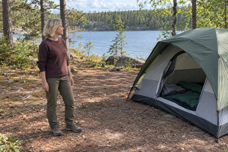 Une femme se tient près d’une tente installée au bord d’un lac.