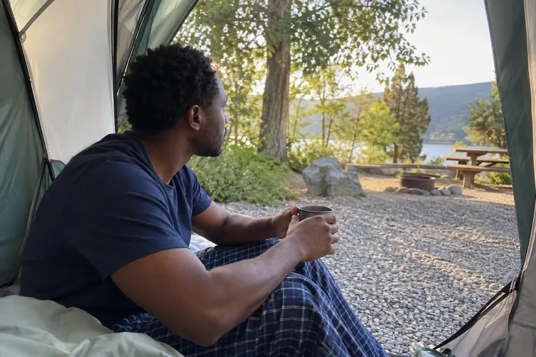Un homme assis à l’entrée d’une tente tient une tasse.