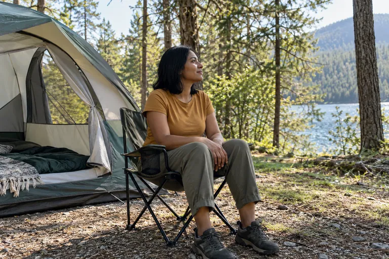 Une femme est assise dans un fauteuil de camping près d’une tente.