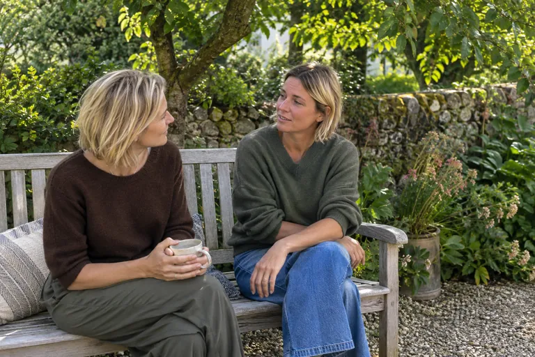 Deux femmes discutent sur un banc de jardin.