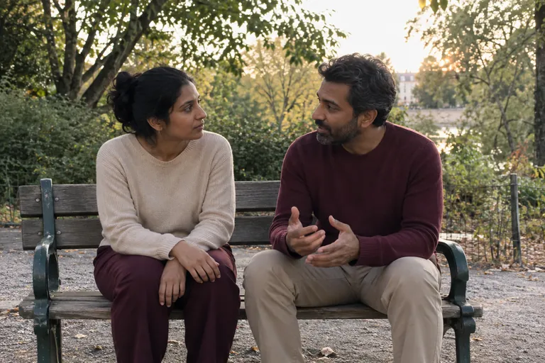 Deux adultes discutent assis sur un banc de parc.