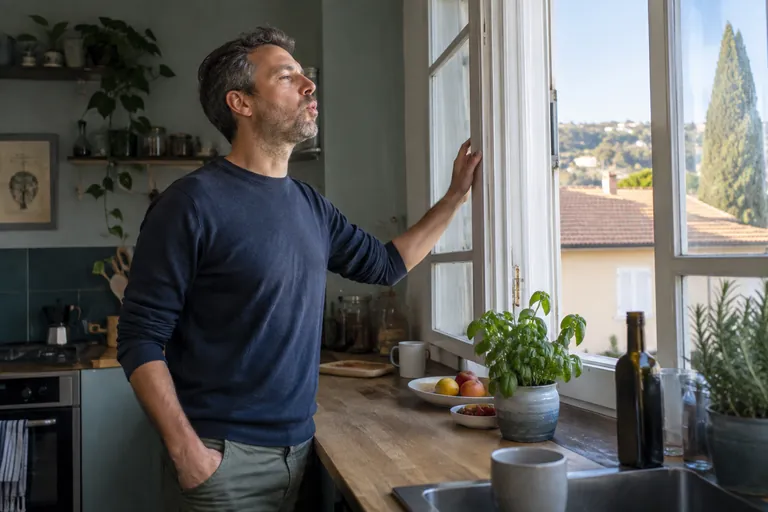 Un homme près d’une fenêtre ouverte expire lentement, les épaules qui se relâchent