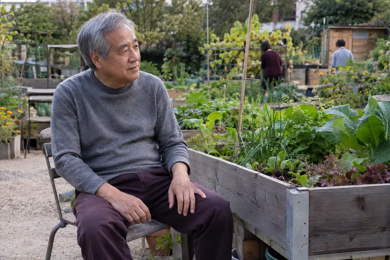 Un homme est assis près d’un bac de culture dans un jardin partagé.