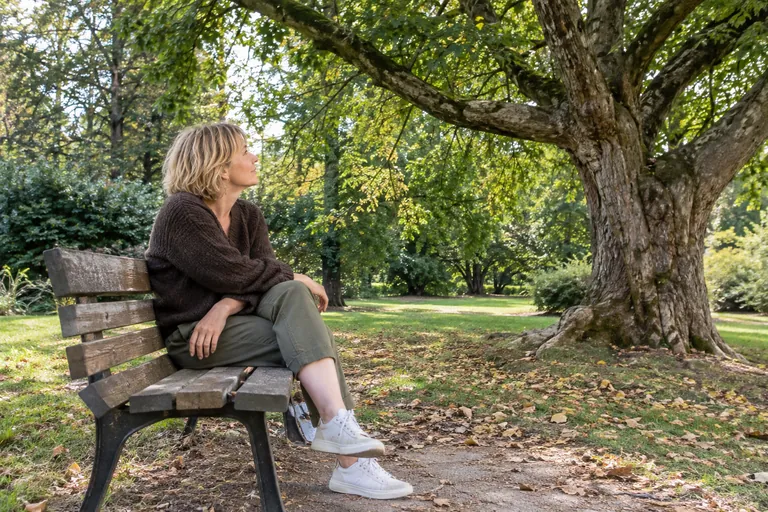 Une femme assise sur un banc regarde les branches d’un arbre.
