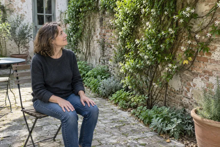 Une femme assise sur une chaise regarde une plante grimpante dans une cour.