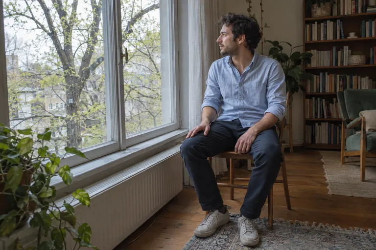 Un homme assis sur une chaise regarde les arbres à travers une fenêtre.