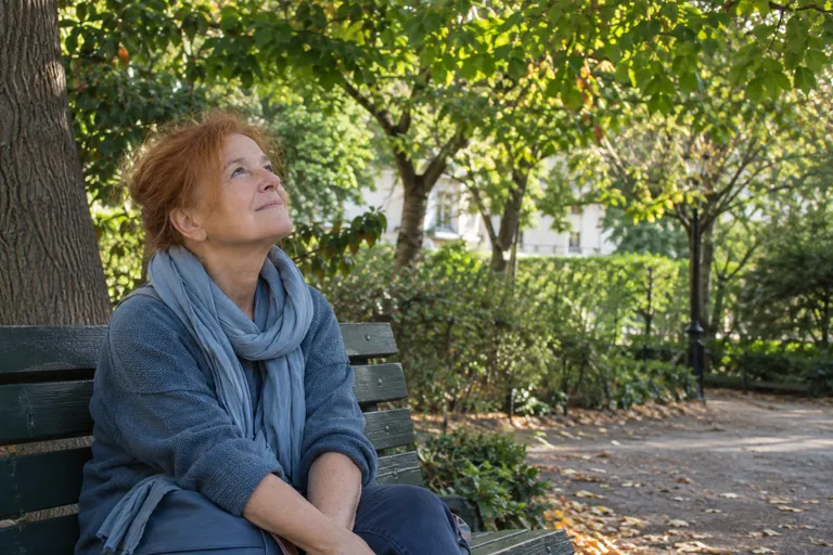 Une femme assise sur un banc regarde les branches des arbres.