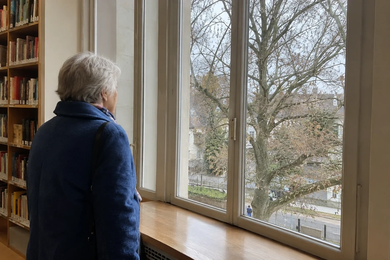 Une femme regarde un arbre depuis une fenêtre de bibliothèque