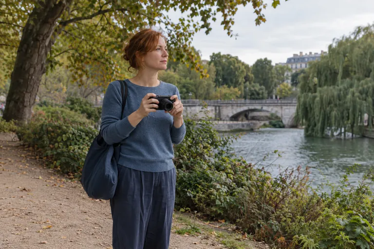 Une femme tient un appareil photo dans un parc au bord de l’eau.