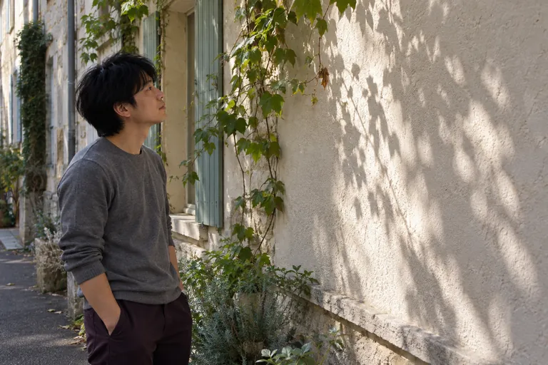 Un homme observe les feuilles d’une plante grimpante et leurs ombres sur un mur.