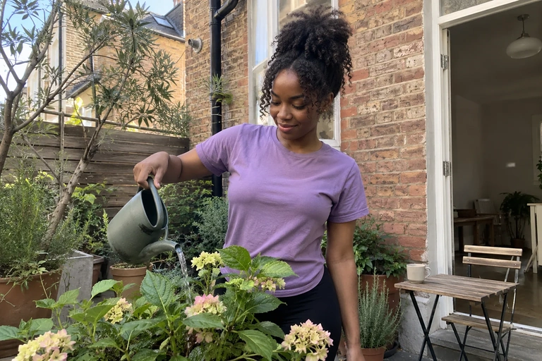 Une femme arrose une plante dans une cour pendant une pause