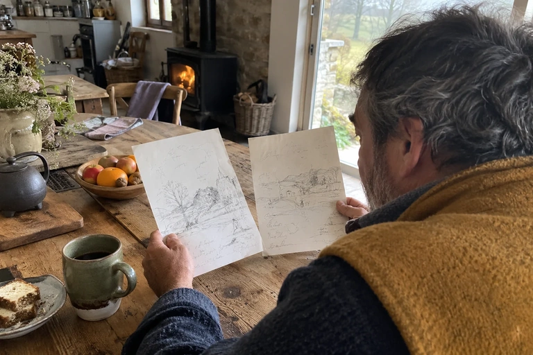 Un homme compare deux croquis tenus au-dessus d’une table