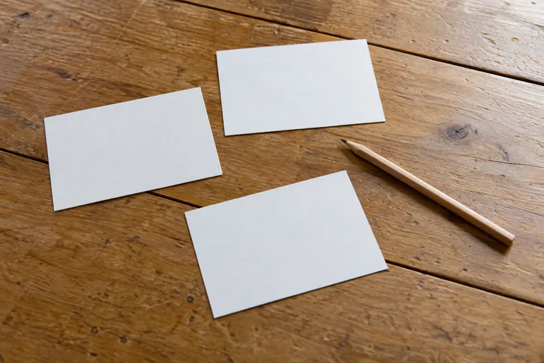 Trois cartes vierges et un crayon sont posés sur une table en bois