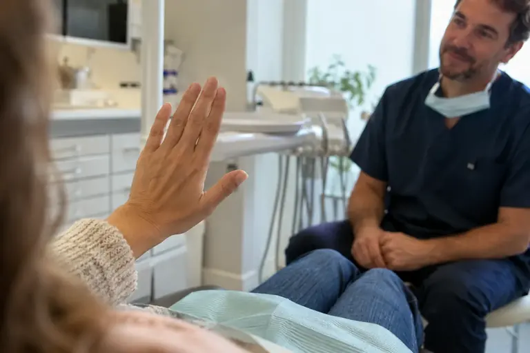La main d’un patient adulte levée doucement pendant une conversation avec un dentiste, avant l’examen