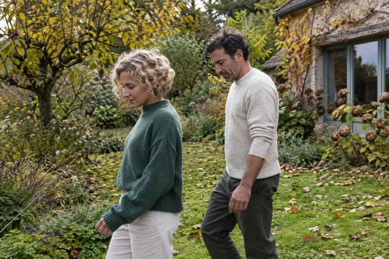 Deux adultes marchent dans un jardin couvert de feuilles.