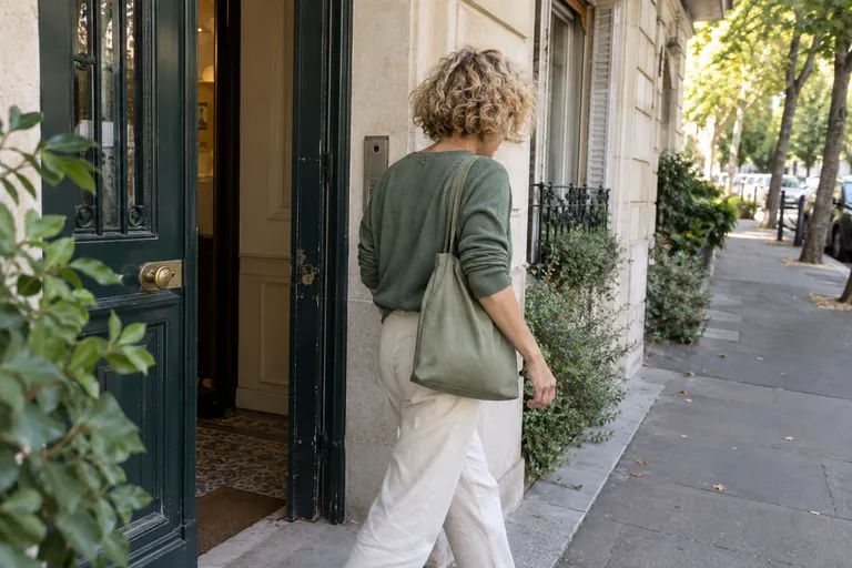 Une femme portant un sac en tissu sort d’un immeuble sur un trottoir.