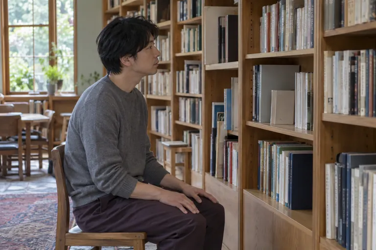 Un homme assis dans une bibliothèque regarde les livres sur une étagère.