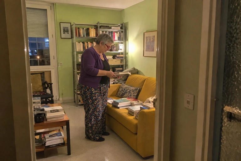 Une femme se tient près d’un canapé avec un livre et une couverture