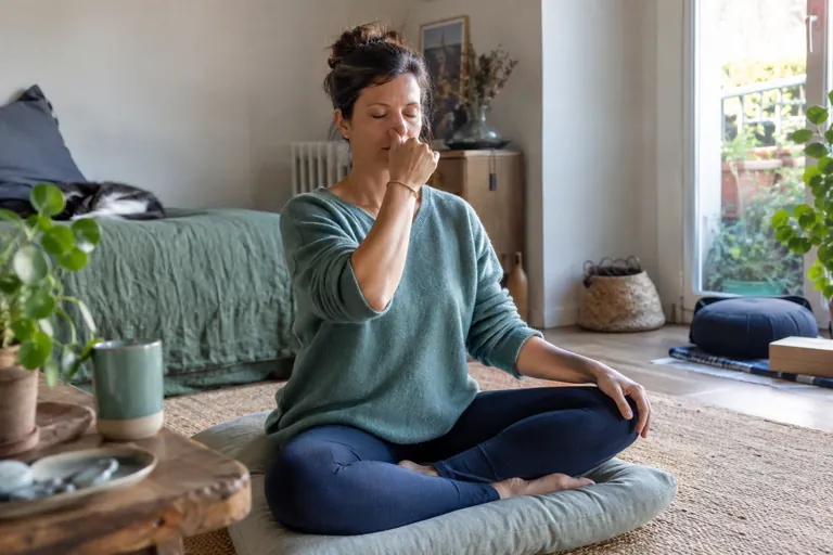 Une femme assise en tailleur pratique la respiration alternée, la main droite près du nez