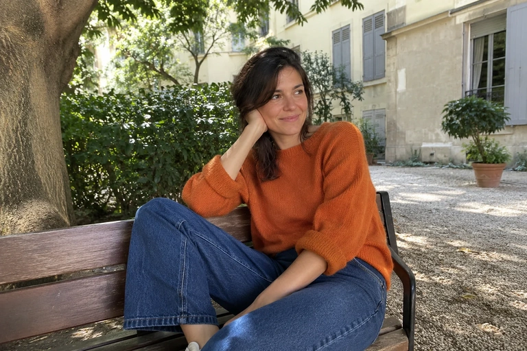 Une femme se repose sur un banc dans une cour ombragée, les yeux ouverts