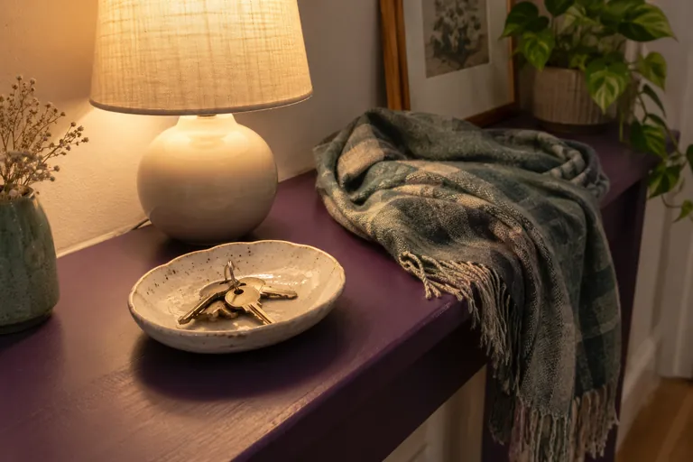 Des clés reposent dans une coupelle près d’une lampe allumée et d’une écharpe.