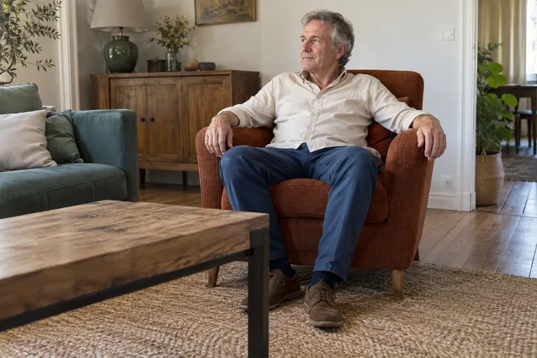 Un homme est assis dans un fauteuil de salon, les mains sur les accoudoirs.