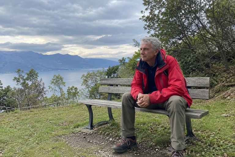 Un homme en veste rouge se repose sur un banc avec vue sur un lac