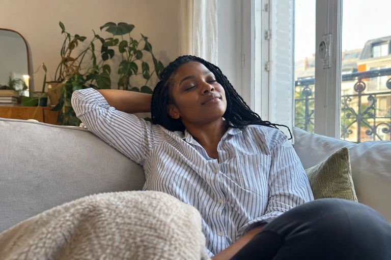 Une femme se repose les yeux fermés sur un canapé près d’une fenêtre