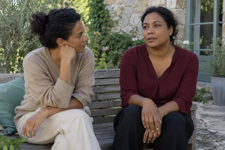 Deux femmes échangent assises sur un banc extérieur.