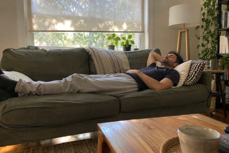Un homme est allongé sur un divan sous une fenêtre ombragée