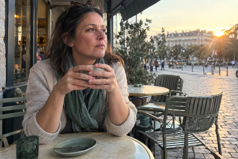 Une femme seule en terrasse de café tient sa tasse à deux mains, le regard dans le vague