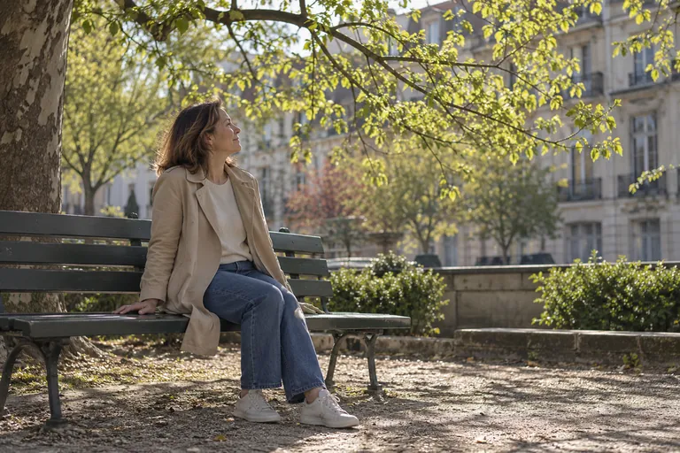 Une femme assise sur un banc regarde les branches d’un arbre.