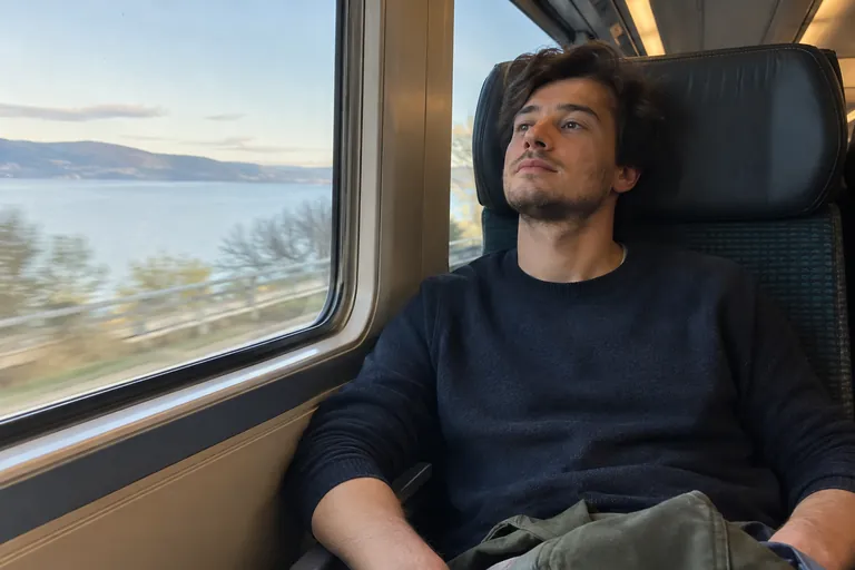 Un jeune homme assis dans un train laisse échapper un long soupir détendu