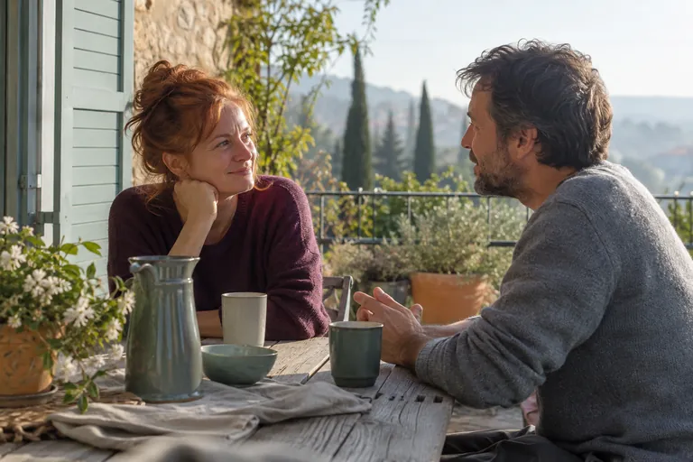 Deux adultes discutent autour de tasses sur une terrasse.