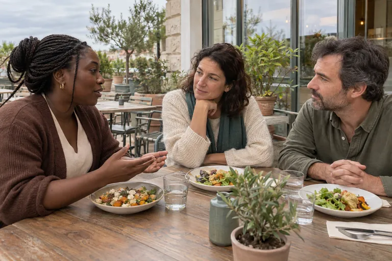 Trois adultes discutent autour d’un repas sur une terrasse.