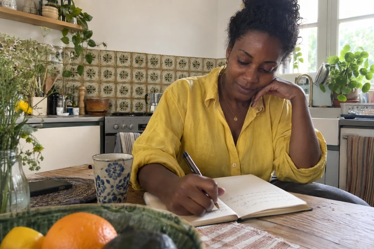 Une femme note quelques éléments dans un carnet à sa table de cuisine
