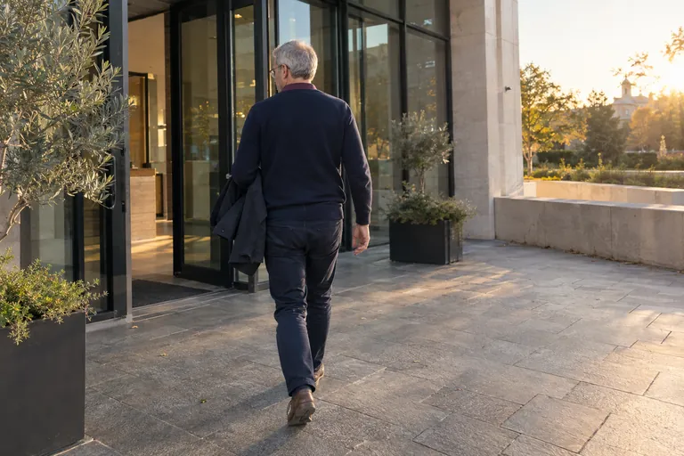 Un homme portant une veste sur le bras marche près d’une porte vitrée.