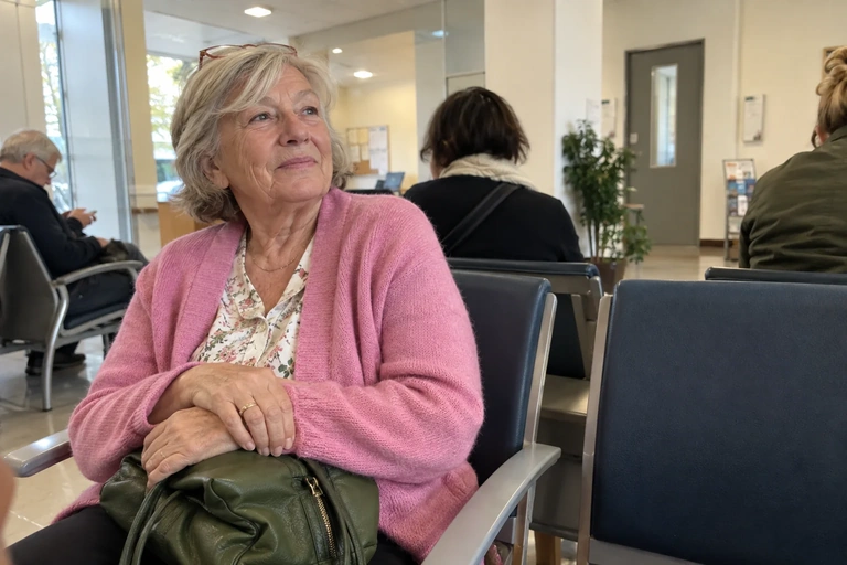 Une femme assise dans une salle d’attente garde les mains sur son sac