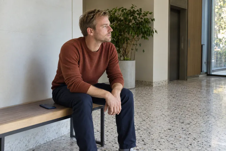 Un homme attend assis sur un banc dans un hall.