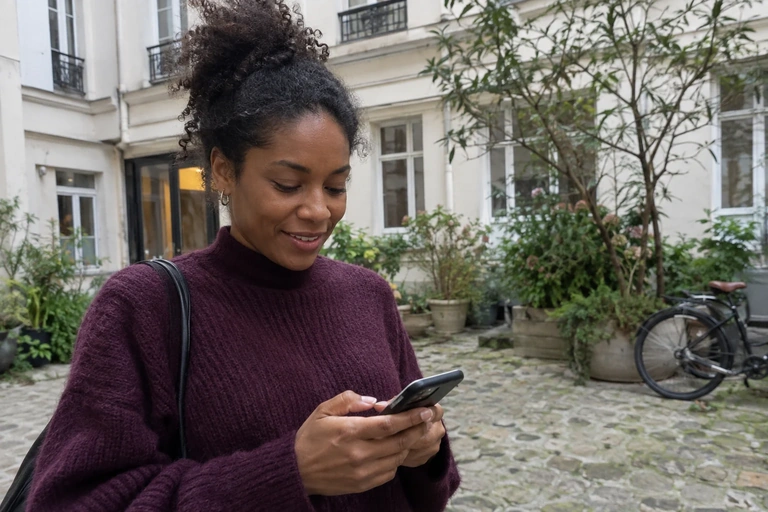 Une femme consulte son téléphone dans une cour d’immeuble