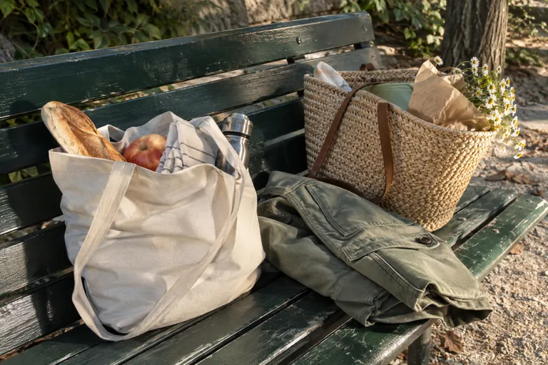 Deux sacs de pique-nique et une veste pliée reposent sur un banc.